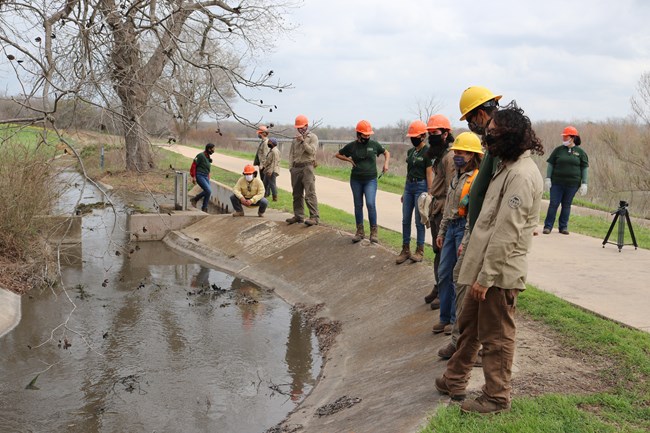 Interns and Apprentices stand in a line along the acquia, an earthen ditch.