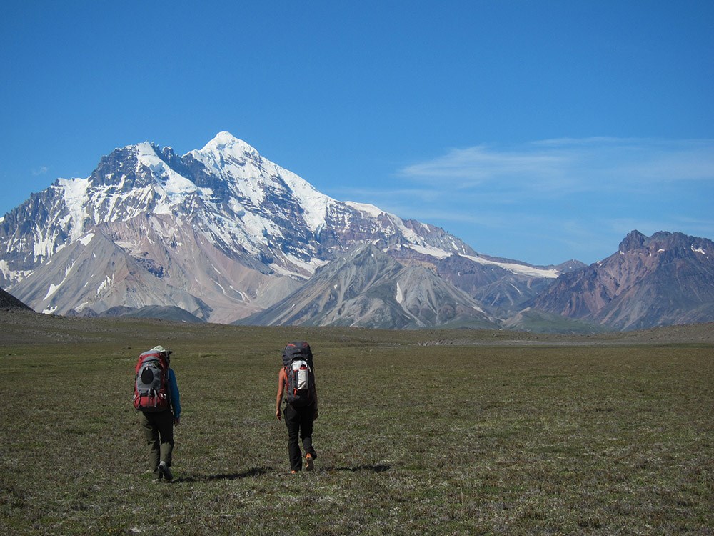 Two people walking toward mountains.