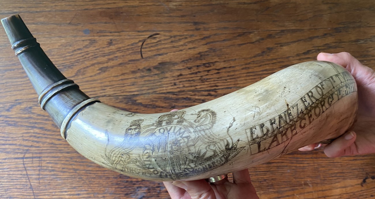 IMG_8415 A large powder horn made of cow bone, with images of the British Royal Coat of Arms and name Ebenezer scratched into the surface