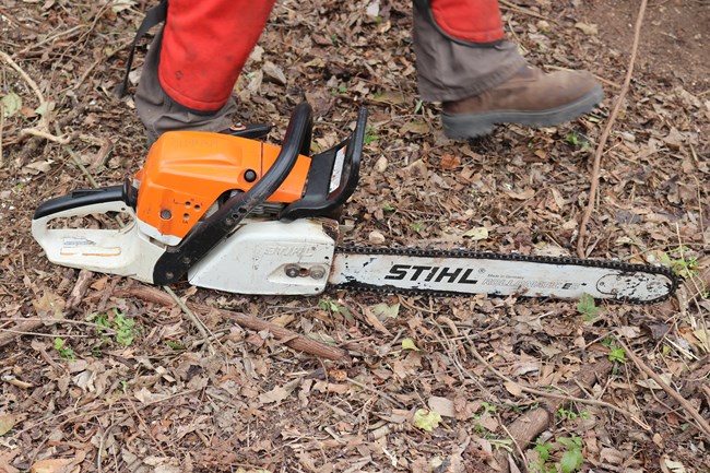 Chainsaw laying on the bare dirt at the historic earthen ditch