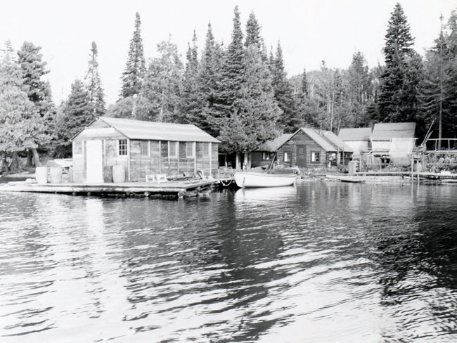 fish house on left over waterway, cabin behind it, net racks on right