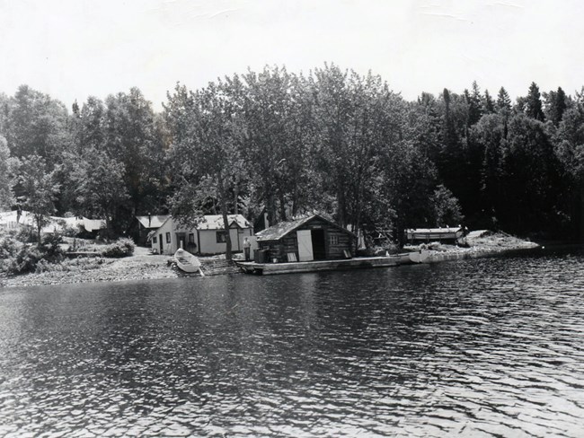 shoreline of fishery, boat pulled up on ramp next to fish house, cabin in back