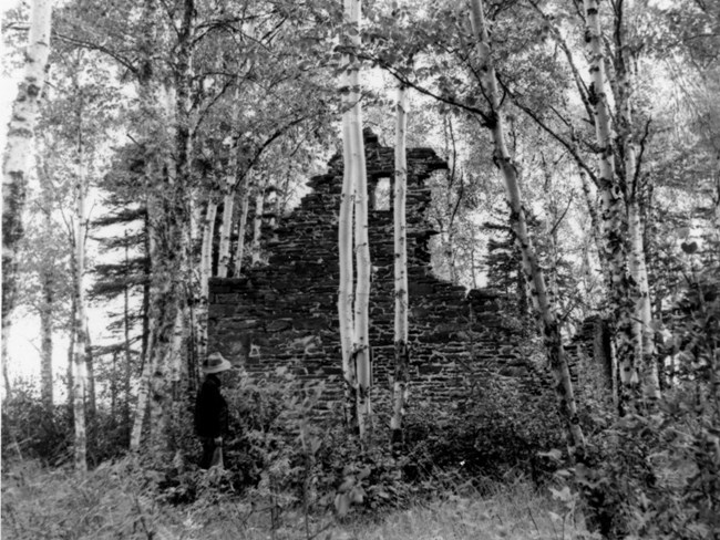 a stone wall stands in ruins, at least 20 feet high, man looks on