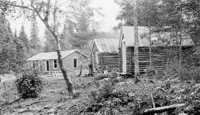 three log cabins with man cutting tree in front