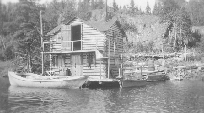 Johnson/Olson Fishery two story, log hewn fish house with dock surrounding it and two boats docked