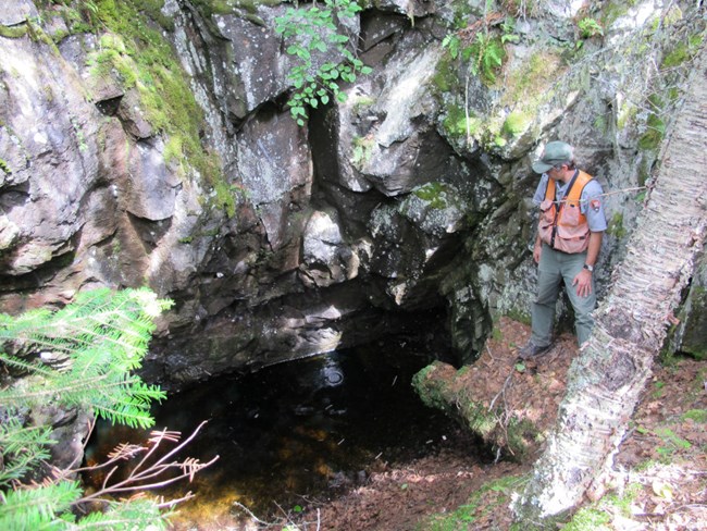 archaeologist looks on at a mine shaft filled with water