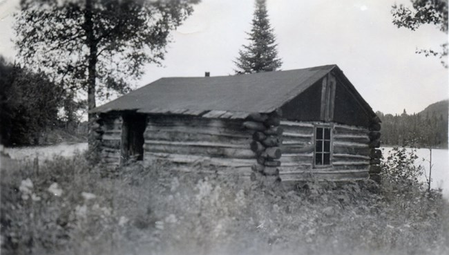 log cabin with front door ajar, water in background