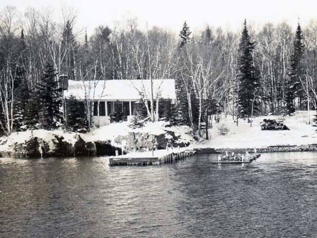 Ralph Cottage cabin with a snow covered roof sits on the snowy banks of Rock Harbor