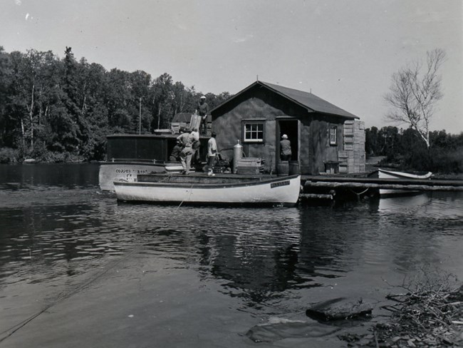 people gathered at fish house, boat unloading empty fish boxes