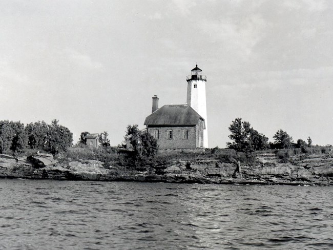 black and white photo shot from the water of the Isle Royale Lighthouse and its outbuilding in 1963
