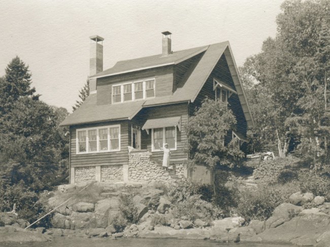 Tallman Cottage ornate two story house overlooking Rock Harbor channel, woman waving from front steps