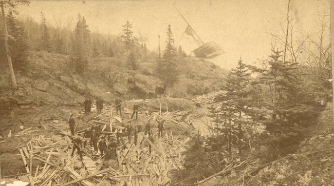 a field of boards scattered amongst the Mott Island rocks, men gather to look at the rubble left of the SS Algoma