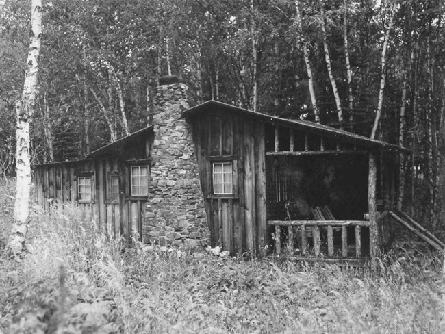 small cabin with log hewn front porch and stone chimney