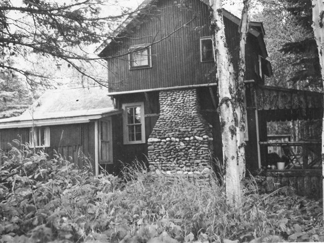 multi level cabin with large covered front porch and stone chimney extending from ground halfway up