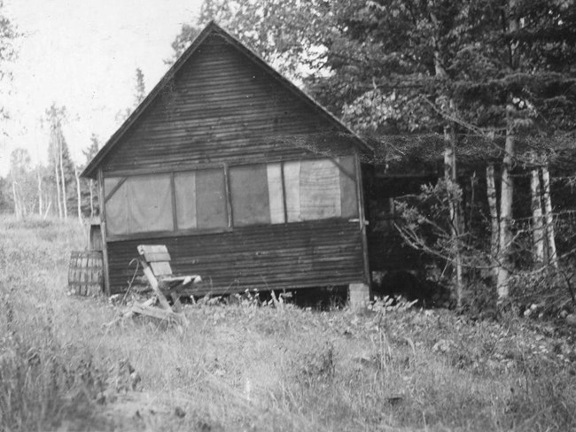 cabin resting on concrete block with large screened windows and chair out front