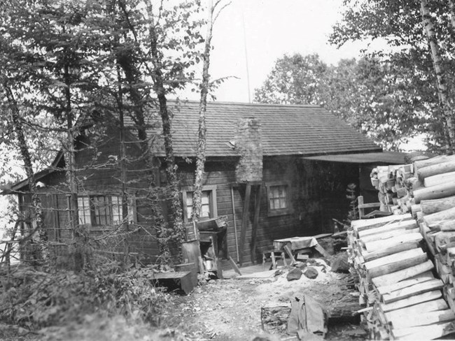wood sided cabin with large log pile in front yard on right
