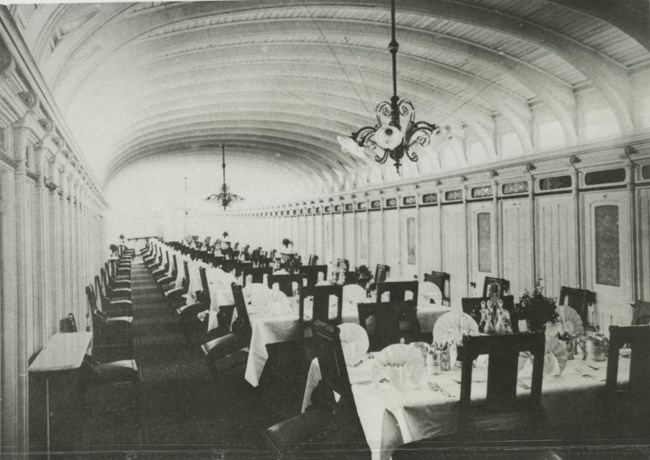 ornate dining room in ship, columned walls, chandeliers overhead, an endless row of white clothed tables