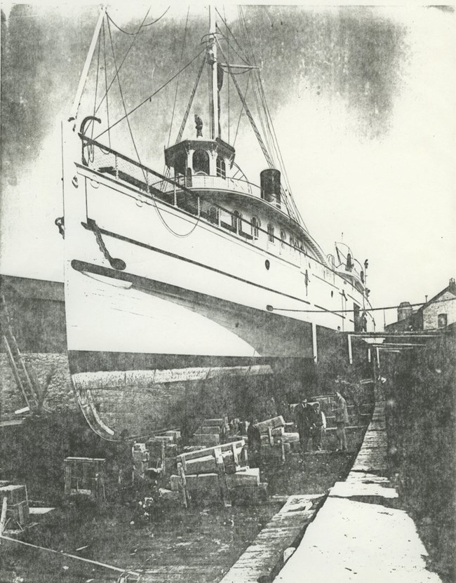 SS Manitoba sitting in drydock with people gathered around ship, likely at end of construction