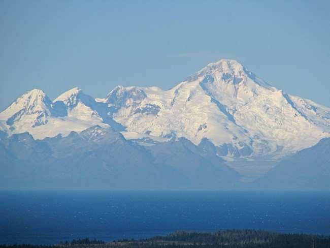 Image of a snow covered stratovolcano with blue skies in the background.