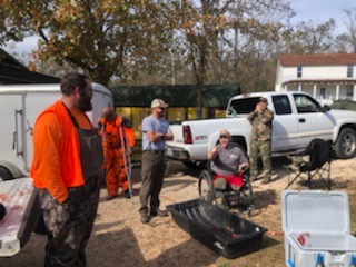 A group of hunters in hunting clothing gathered around vehicles before a hunt.