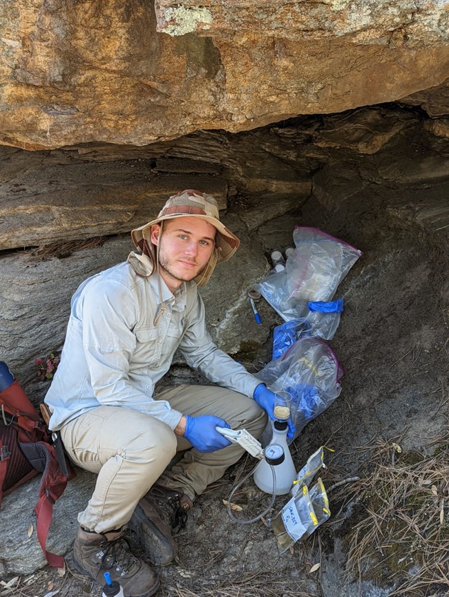 Wesley crouched down under a rock overhang with his equipment