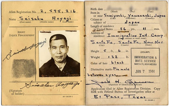 Pages of a document booklet. On the left, a black and white photo of a Japanese man with short hair, a fingerprint, and a signature. On the right are his identifying characteristics including height, weight, and the presence of a small mole.
