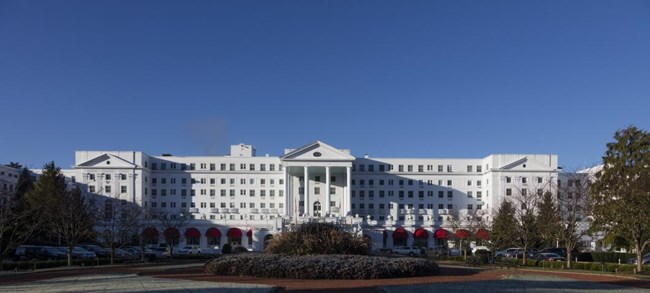 Color photo of a large, bright white hotel with 6 stories against a bright blue sky.