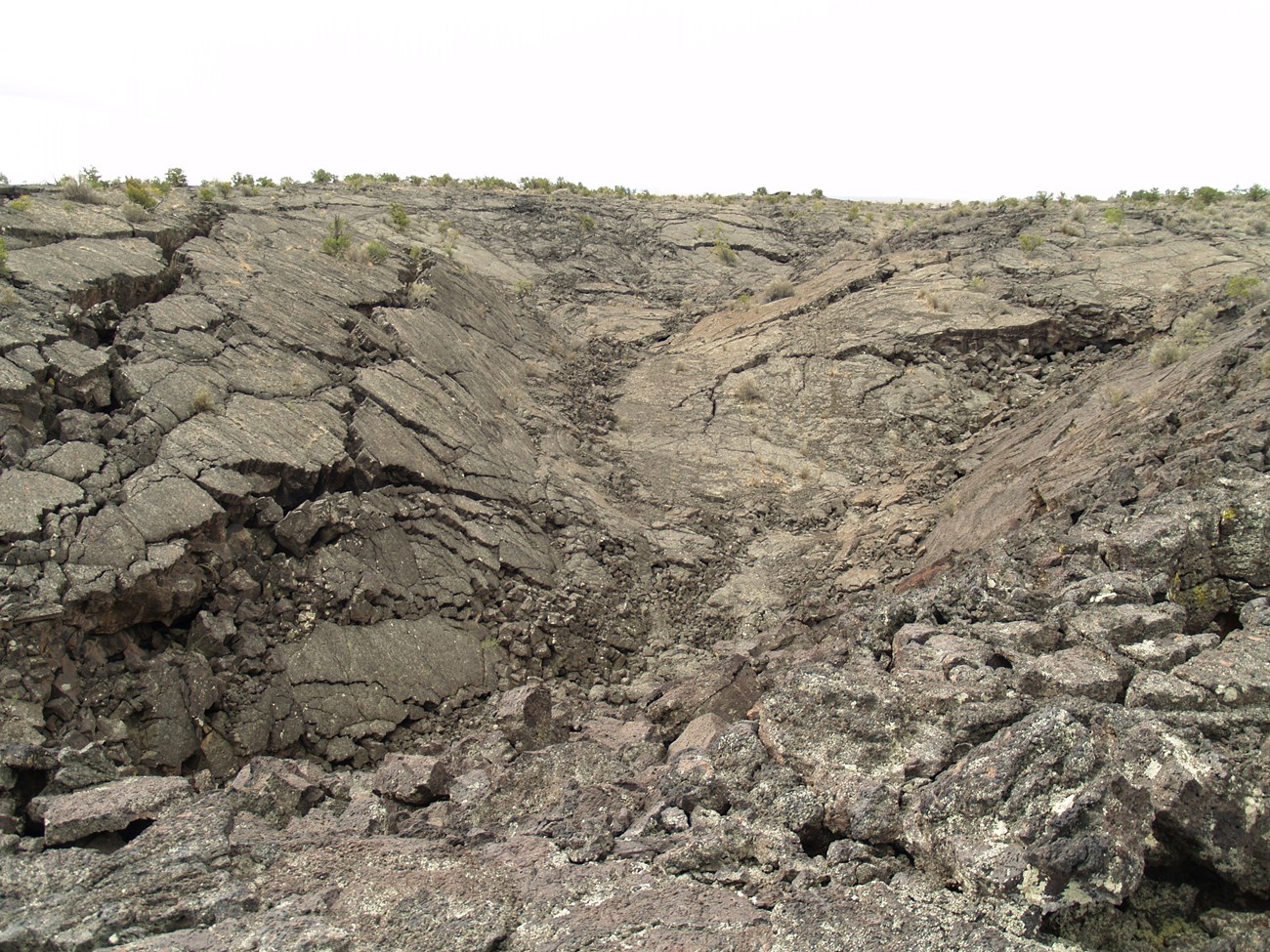 Photo of landscape covered with lava rock that has pits and cracks.