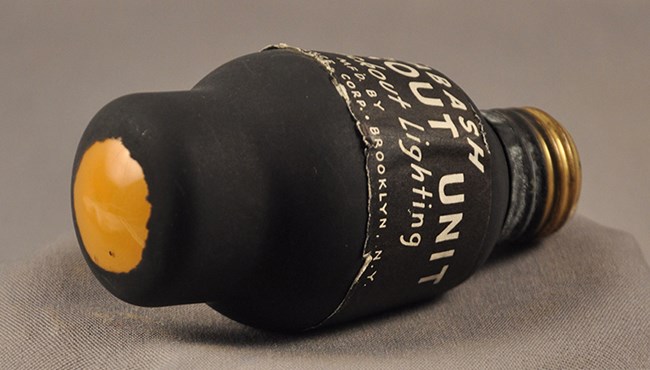 Color photo of a lightbulb that is painted black and has a “Wabash Blackout Unit” label on it.