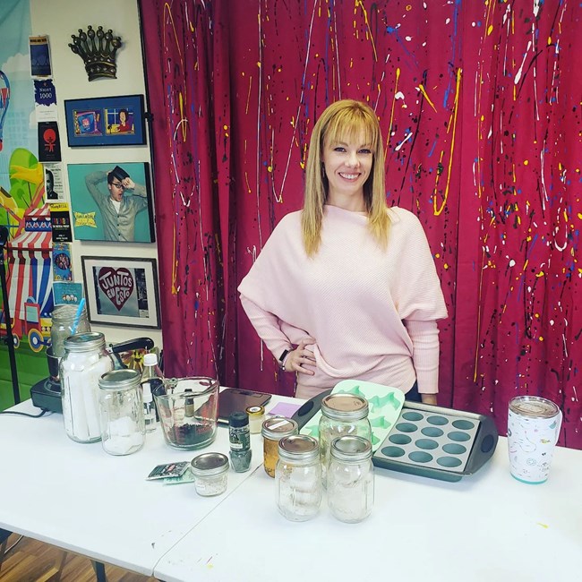 Izzy-Anderson-e1566053448126-200x300 A woman with blonde hair smiles at us while standing at an art table.