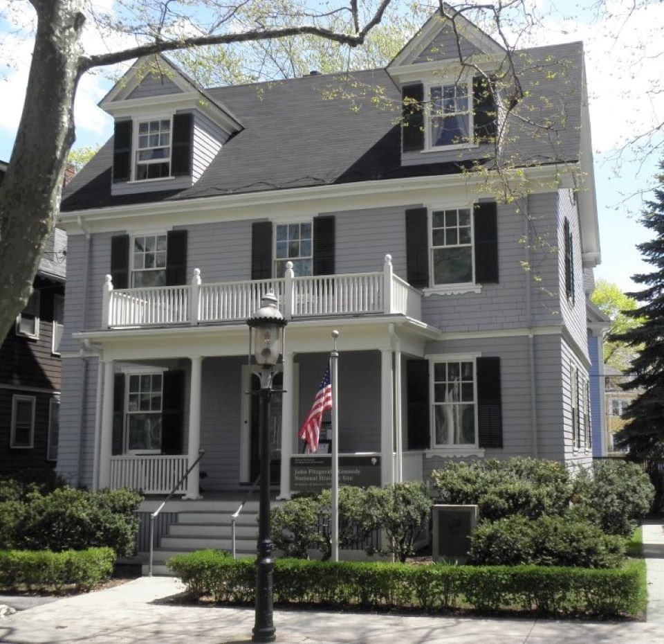 Grey house on a tree-lined street. US Flag on pole. Street light in front.