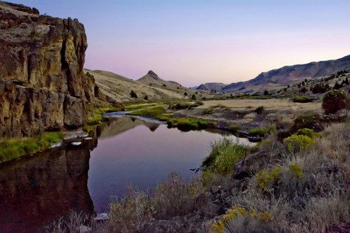 A photograph of a calm river with a cliff on the left and the pyramid shape of Sheep Rock in the distance A photograph of a calm river with a cliff on the left and the pyramid shape of Sheep Rock in the distance