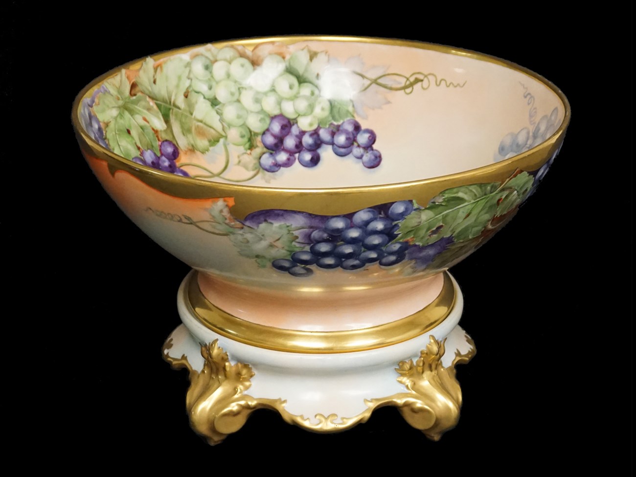 Peach colored bowl on stand with decoration of bunches of grapes