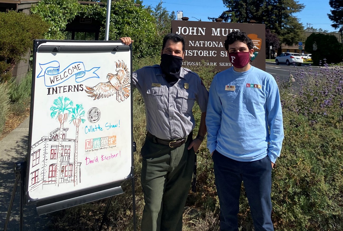 Park Ranger and David Escobar standing next to a sign decorated to welcome interns to John Muir National Historic Site