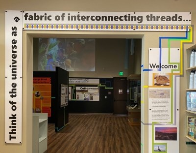 A photo of the entrance to an exhibit area framed with the words "Think of the universe as a fabric of interconnecting threads..."