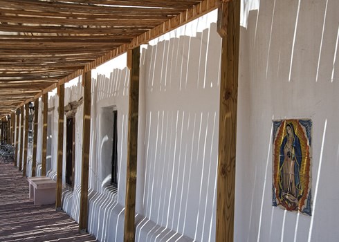 Sunlight slices through the slats of a wood portal in the San Elizario Historic District, accenting the town’s beauty as a center of historic adobe architecture and an inviting visitor’s experience. Photo © Jack Parsons
