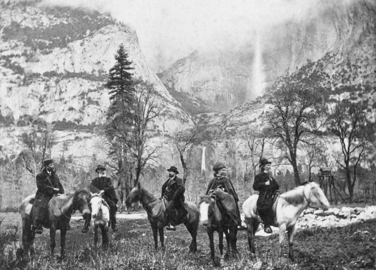 Five people on horseback in a field in front of Yosemite Falls.