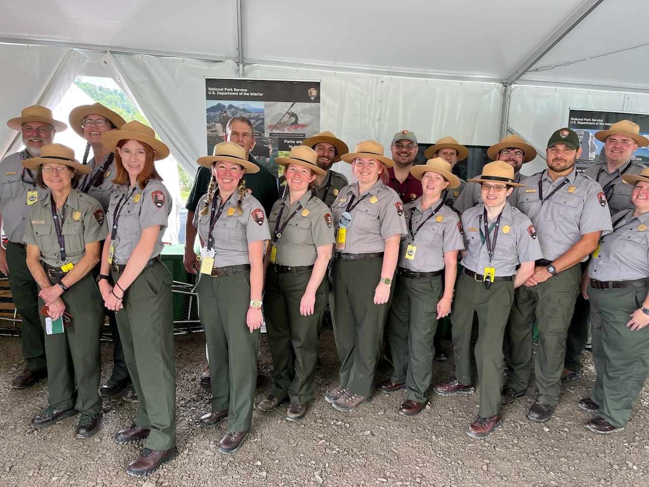 Jamboree Group 17 staff dressed in green pants and gray shirts, with gold badges, and the NPS logo. Most are wearing a flat hat with some in ball caps, and one without a hat.