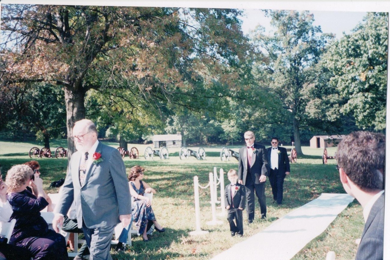 A small child and two adults all dressed in fancy attire walk down the aisle