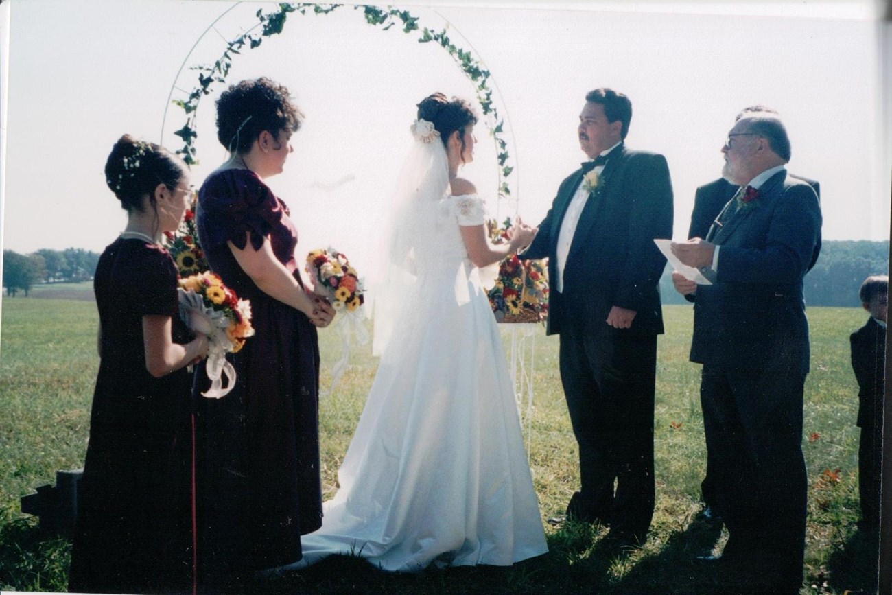 A bride, groom, and small wedding party stand in a field.