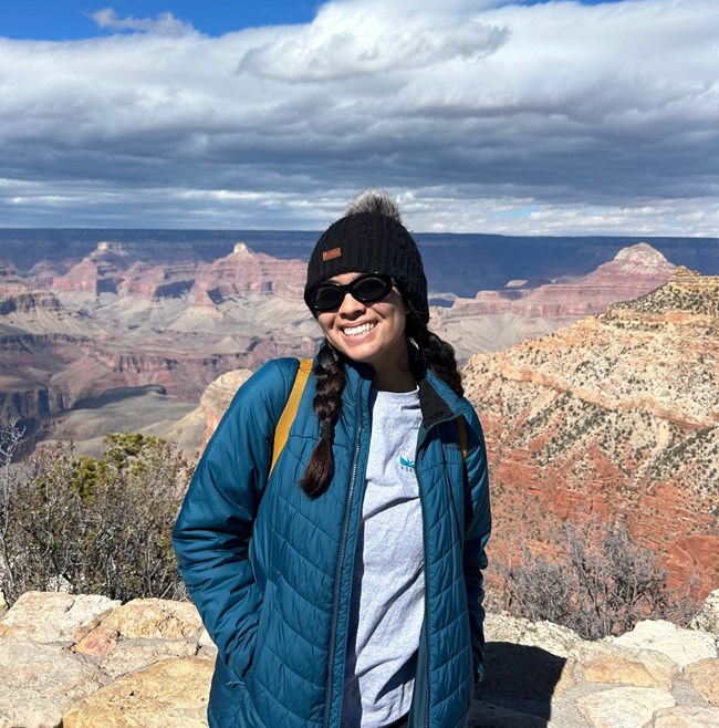 Virginia Javier Woman with warm hat and coat smiles as she poses for a photo near a beautiful deep redrock canyon.