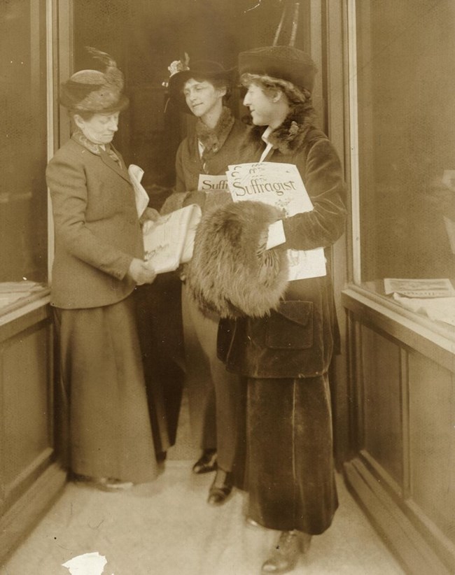 Three woman standing in a group holding copies of a newspaper LOC