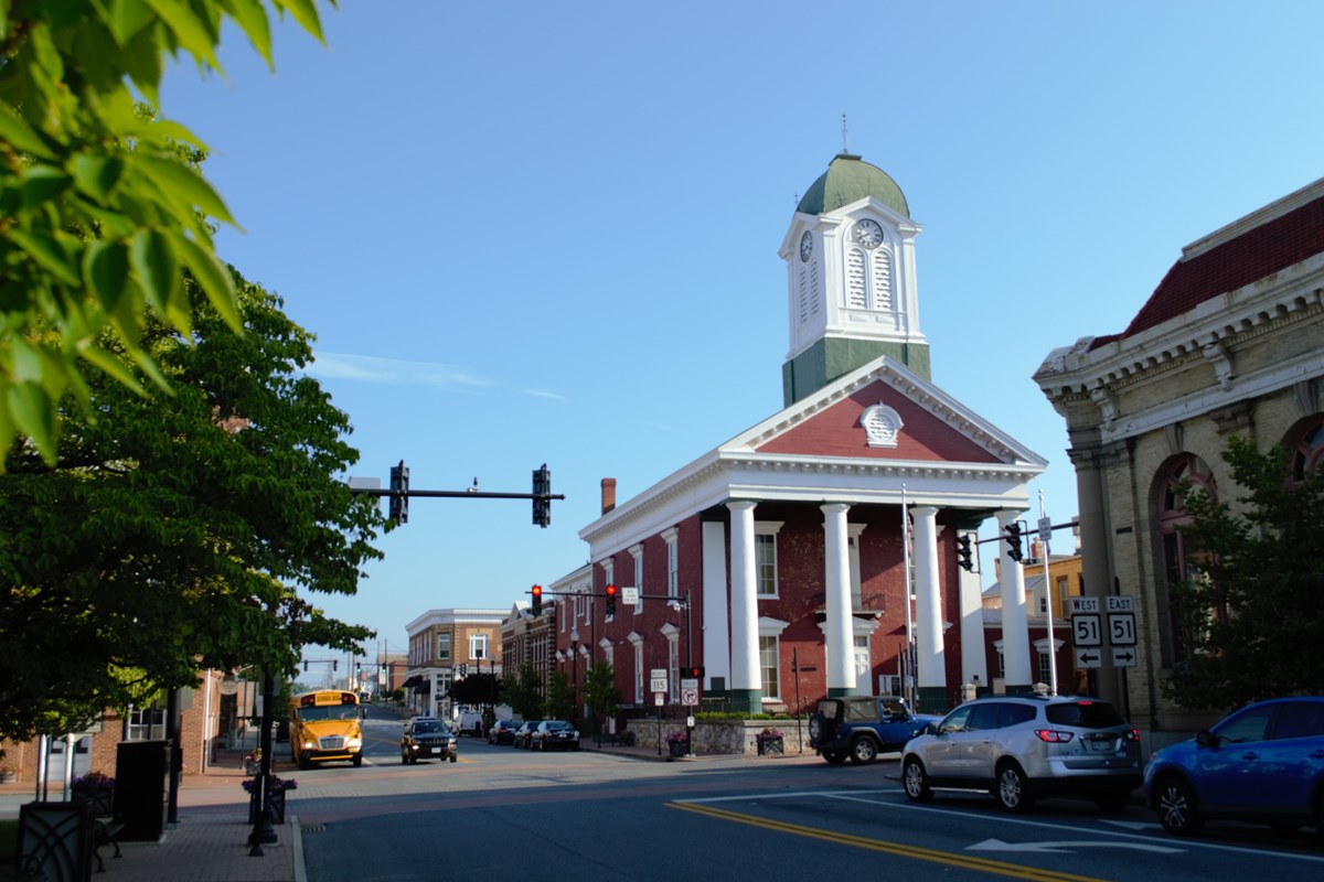 Red brick building with a columnated portico and a green and white clocktower rising from the center.