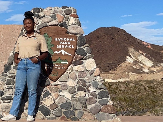Jenelle_Booker Woman wearing jeans and internship T-shirt smiling near Lake Mead National Recreation Area sign.