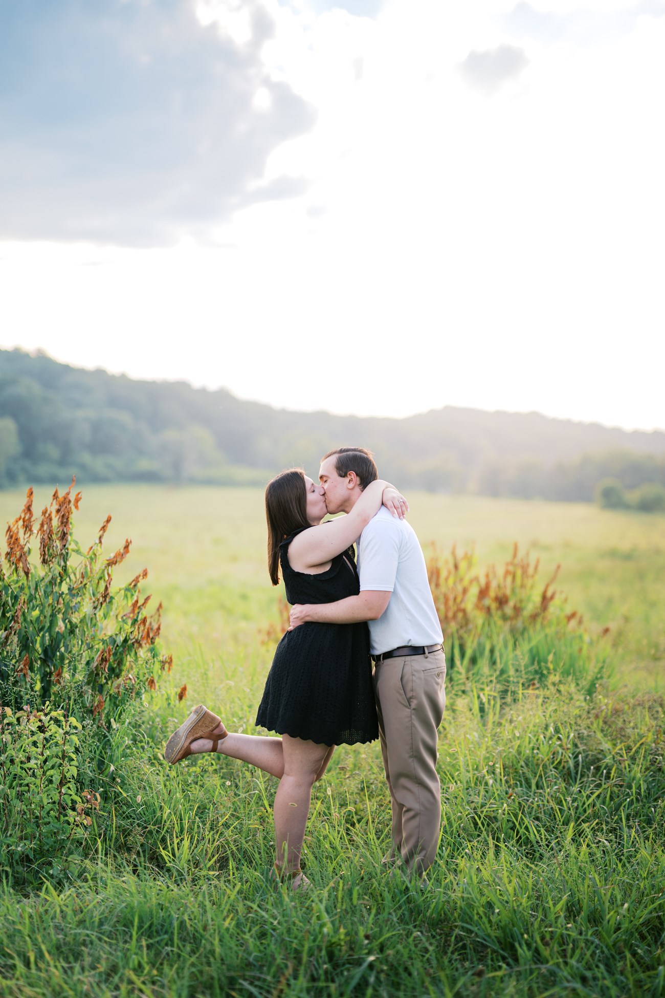 A couple kiss in a field.