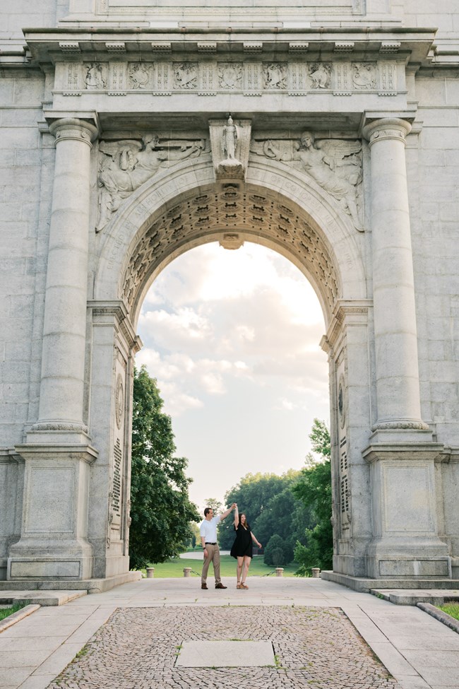 A couple dance under a large stone arch.