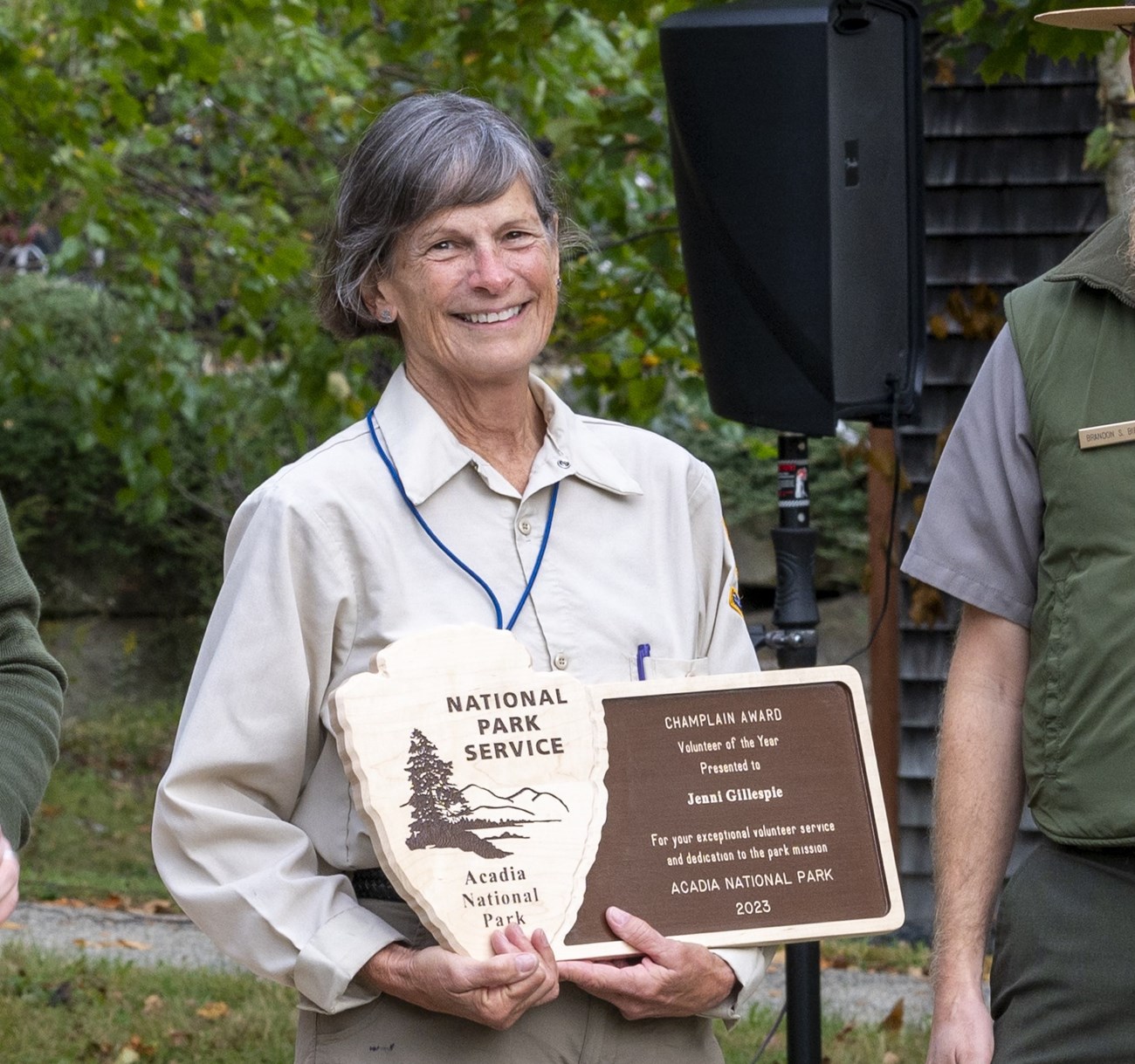 Jennifer holding her Volunteer of the Year award. A woman with salt and pepper hair and dressed in the NPS volunteer uniform holds a wooden plaque decorated with the National Park arrowhead logo and the text "Volunteer of the Year: 2023"