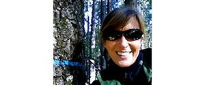 Headshot of a woman next to a tree in a forest.