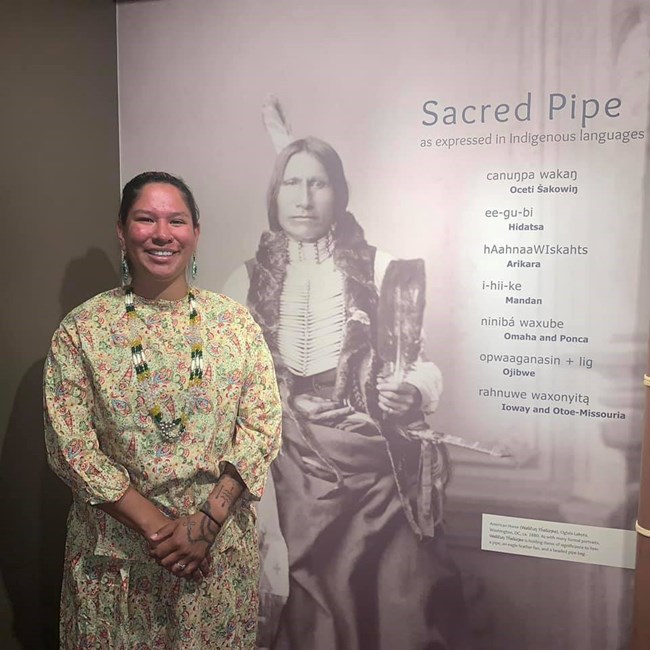 Jessica Arkeketa next to a sign that says, "Sacred Pipe"