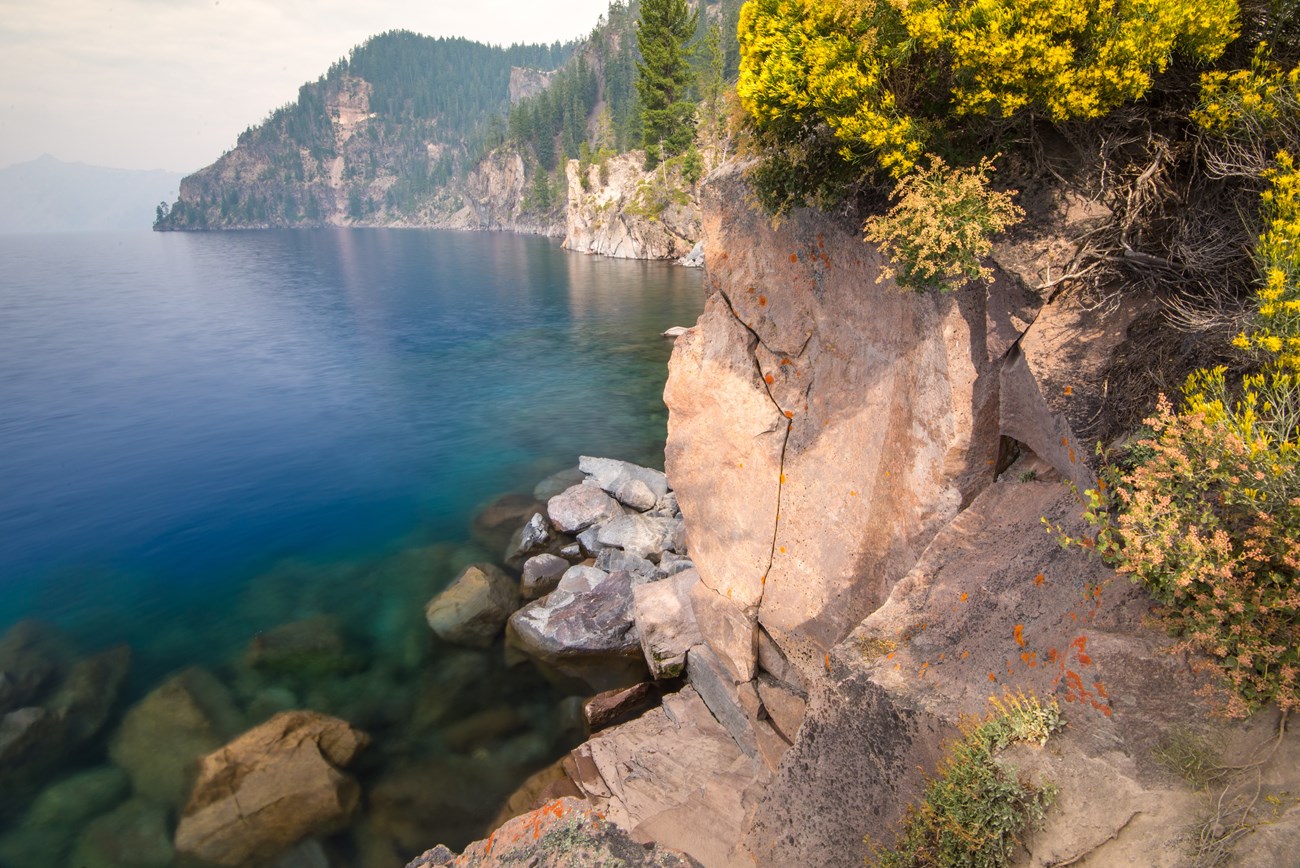 Rocky cliff with yellow shrubbery above large lake.